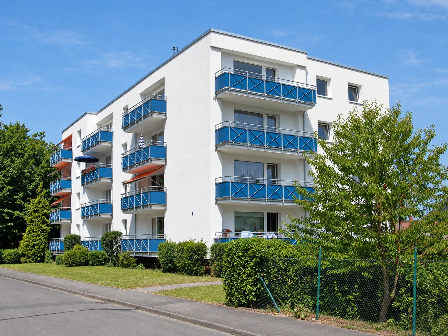 Saniertes Mehrfamilienhaus mit weißer Fassade und blauen Balkonbrüstungen