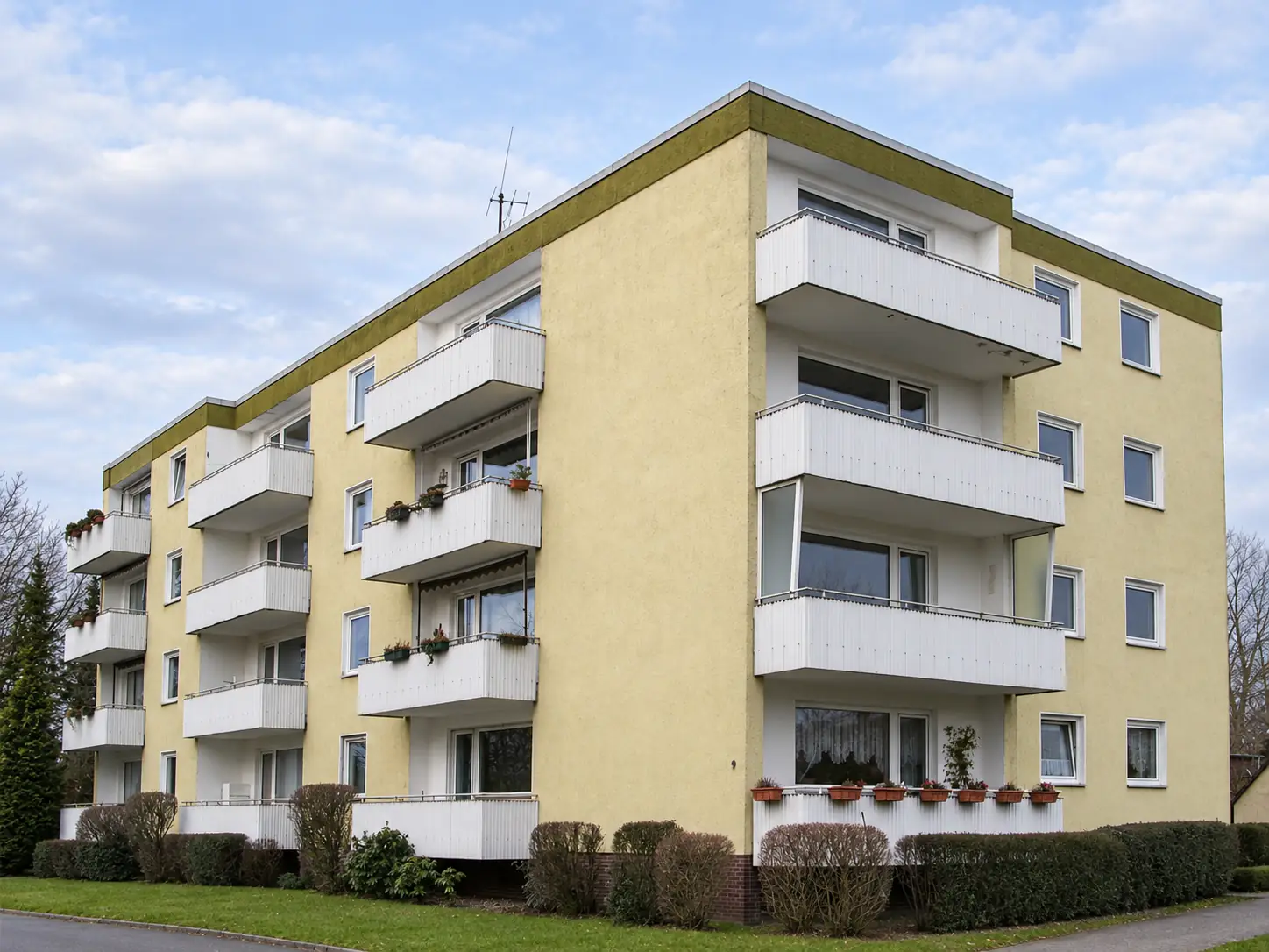 Mehrfamilienhaus vor der Sanierung mit gelber Fassade und weißen Balkonbrüstungen