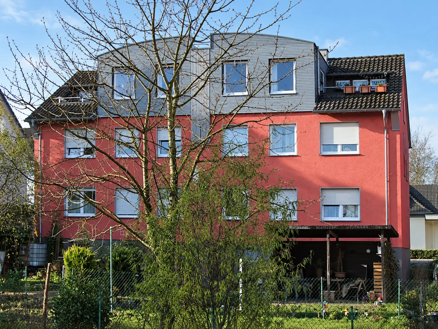 Saniertes Wohngebäude mit roter Fassade und großem Dachaufbau