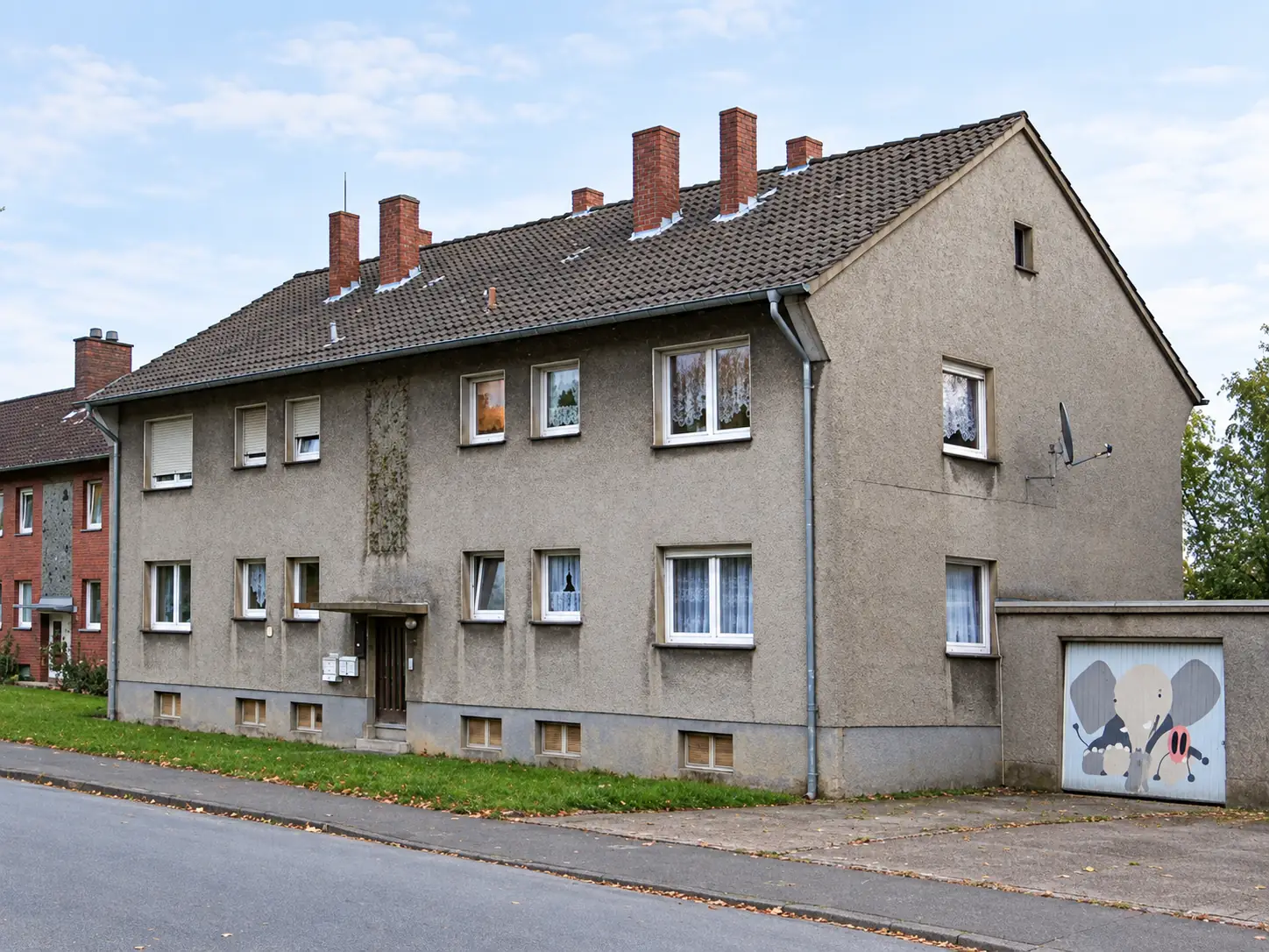 Wohngebäude im Bestand mit grauer Putzfassade und geneigtem Dach